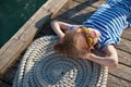 Beautiful little girl in sunglasses and sailor stripes shirt lying on rope and wooden pier Royalty Free Stock Photo