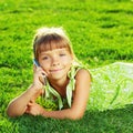 Beautiful little girl is talking on a phone and lying on a green