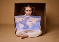 Beautiful little girl with two ponytails sitting inside a cardboard box with a poster- a painted image with World map, Royalty Free Stock Photo