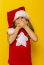 Little girl wearing Santa hat holding hands over mouth Royalty Free Stock Photo