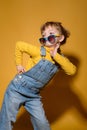 Beautiful little girl wearing stylish denim overall, roll neck jumper and lowered colorful sunglasses posing playfully on bright Royalty Free Stock Photo