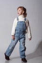 Beautiful little girl wearing stylish denim overall, white roll neck fluffy jumper posing on white background Royalty Free Stock Photo