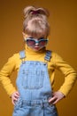 Beautiful little girl wearing stylish denim overall, yellow roll neck jumper and colorful sunglasses Royalty Free Stock Photo