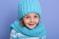 Beautiful little girl wearing winter warm turquoise cap and scarf poding over purple background in studio, female child can not Royalty Free Stock Photo