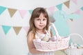 Beautiful little girl in a white dress is standing with an Easter basket. Many different colorful Easter eggs, colorful interior.