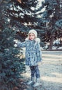 The beautiful little girl in winter wood. The girl is dressed in a gray fur coat. She is holding a white Christmas ball