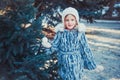 The beautiful little girl in winter wood. The girl is dressed in a gray fur coat. She is holding a white Christmas ball