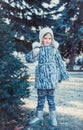 The beautiful little girl in winter wood. The girl is dressed in a gray fur coat. She is holding a white Christmas ball