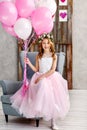 A beautiful little girl in a wreath of fresh flowers and an elegant pink dress celebrates her birthday in a white studio Royalty Free Stock Photo