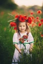 Beautiful little girl with a wreath of poppies in a white dress and collects a bouquet of wildflowers. cute child in poppy field Royalty Free Stock Photo