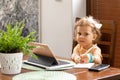 Beautiful little girl 3 years old with curly hair is sitting at table and receiving educational language lessons on tablet. early Royalty Free Stock Photo