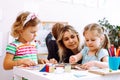 Beautiful little girls with interest fold colored cubes on desk in playroom of kindergarten. Young educator sitting with