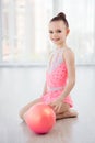 Beautiful little gymnast girl in pink sportswear dress, performing art gymnastics element with ball in fitness class Royalty Free Stock Photo