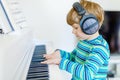 Beautiful little kid boy with headphones playing piano in living room or music school. Preschool child having fun with Royalty Free Stock Photo