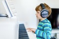 Beautiful little kid boy with headphones playing piano in living room or music school. Preschool child having fun with Royalty Free Stock Photo