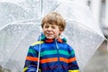 Little blond kid boy on way to school walking during sleet, rain and snow with an umbrella on cold day Royalty Free Stock Photo