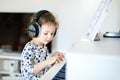 Beautiful little kid girl playing piano with headphones in living room or music school. Preschool child having fun with Royalty Free Stock Photo