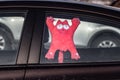 Beautiful little plush soft red toy cat with white eyes and a smile is hanging on the window inside a dirty car