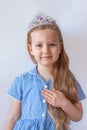 Beautiful little princess girl in silver crown holding magic wand smiling. Young lady with long wavy hair in blue dress Royalty Free Stock Photo