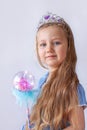 Beautiful little princess girl in silver crown holding magic wand smiling. Young lady with long wavy hair in blue dress Royalty Free Stock Photo