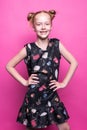 Beautiful little redhead girl in dress posing like model on pink background.