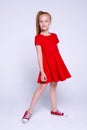 Beautiful little redhead girl in red dress and sneakers posing like model on white background. Royalty Free Stock Photo