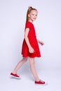 Beautiful little redhead girl in red dress and sneakers posing like model on white background. Royalty Free Stock Photo