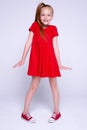 Beautiful little redhead girl in red dress and sneakers posing like model on white background. Royalty Free Stock Photo