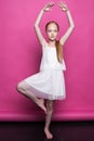Beautiful little redhead girl in white dress posing like model on pink background.