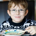 Beautiful little school boy eating vegetable soup indoor. Blond child in domestic kitchen or in school canteen. Cute kid Royalty Free Stock Photo