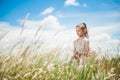 Beautiful little thin girl in summer dress in grass field under blue cloudy sky during leisure activity