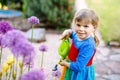 Beautiful little toddler girl in yellow rubber boots and colorful dress watering spring flowers with kids water can Royalty Free Stock Photo