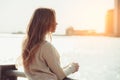 Beautiful lonely girl dreaming and thinking while waiting for date in the city ocean pier at sunset time.