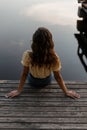 Beautiful lonely young woman in fashion blue jeans with yellow top blouse sits on a wooden pier near the sea Royalty Free Stock Photo