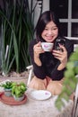 Cute asian girl looking to smartphone in her hand while enjoy the tea Royalty Free Stock Photo