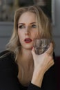 A beautiful long haired blonde sits and rests at a table in a cafe, holding a glass of drink and looking out the window. Royalty Free Stock Photo