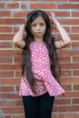 long-haired Colombian girl adjusts her hair next to a brick wall