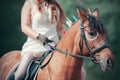 A girl in an american indian suit sits on a Bay horse, decorated with feathers