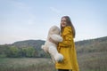Beautiful long-haired girl laughs and plays with teddy bear on autumn day. Young woman in yellow jacket walks in nature Royalty Free Stock Photo