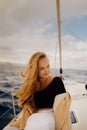 A beautiful long-haired girl sits on the bow of a barred yacht and enjoys life. The blonde is resting in the open sea or ocean.