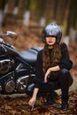 A beautiful long-haired woman smoking on a chopper motorcycle in autumn landscape.