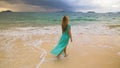 Woman walks to the stormy cloudy ocean on sand beach. Girl in blue swimsuit dress tunic. Concept rest in sea, tropical Royalty Free Stock Photo