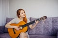 Beautiful long-haired young woman with positive mental health smiling, playing her favorite song on acoustic guitar, sitting on Royalty Free Stock Photo