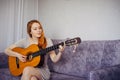 Beautiful long-haired young woman with positive mental health smiling, playing her favorite song on acoustic guitar, sitting on Royalty Free Stock Photo