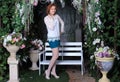 Beautiful long legged redhead girl in green minidress and white fishnet stockings posing at the flowers Royalty Free Stock Photo