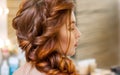 Beautiful, with long, red-haired hairy girl, hairdresser weaves a French braid, in a beauty salon. Royalty Free Stock Photo