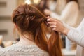 Beautiful, with long, red-haired hairy girl, hairdresser weaves a French braid, in a beauty salon. Royalty Free Stock Photo