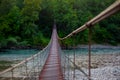 Beautiful, long suspension bridge over a mountain river, going into a dense forest