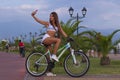 Beautiful longhaired young woman with a bicycle has fun, uses a smartphone, makes selfy on a smartphone