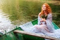 Beautiful longing young sexy woman, redhead with red hair, bride, with a bouquet of flowers in a boat Royalty Free Stock Photo